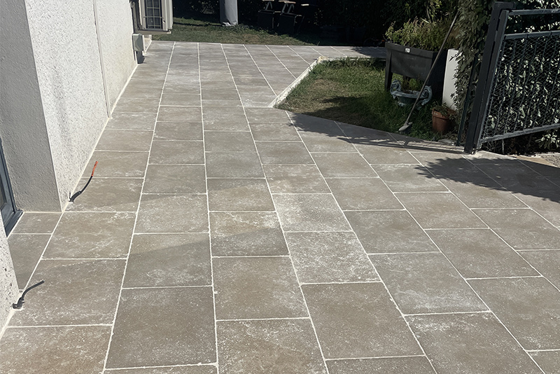 Allée et terrasse réalisées en dalles de pierres grises autour d'une maison.