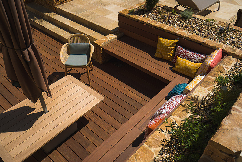 Terrasse en bois avec banc intégré accollée à une maison.