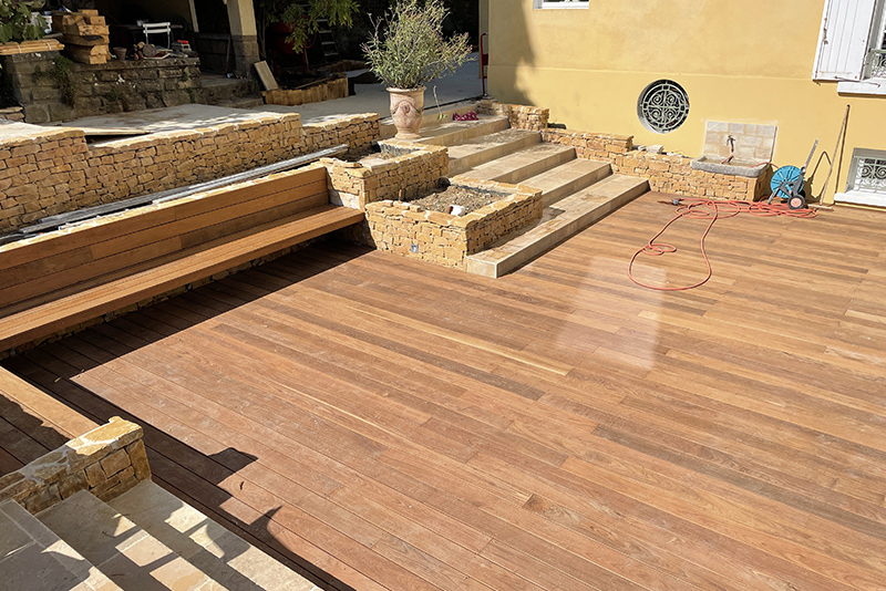 Terrasse en bois avec banc intégré accollée à une maison.